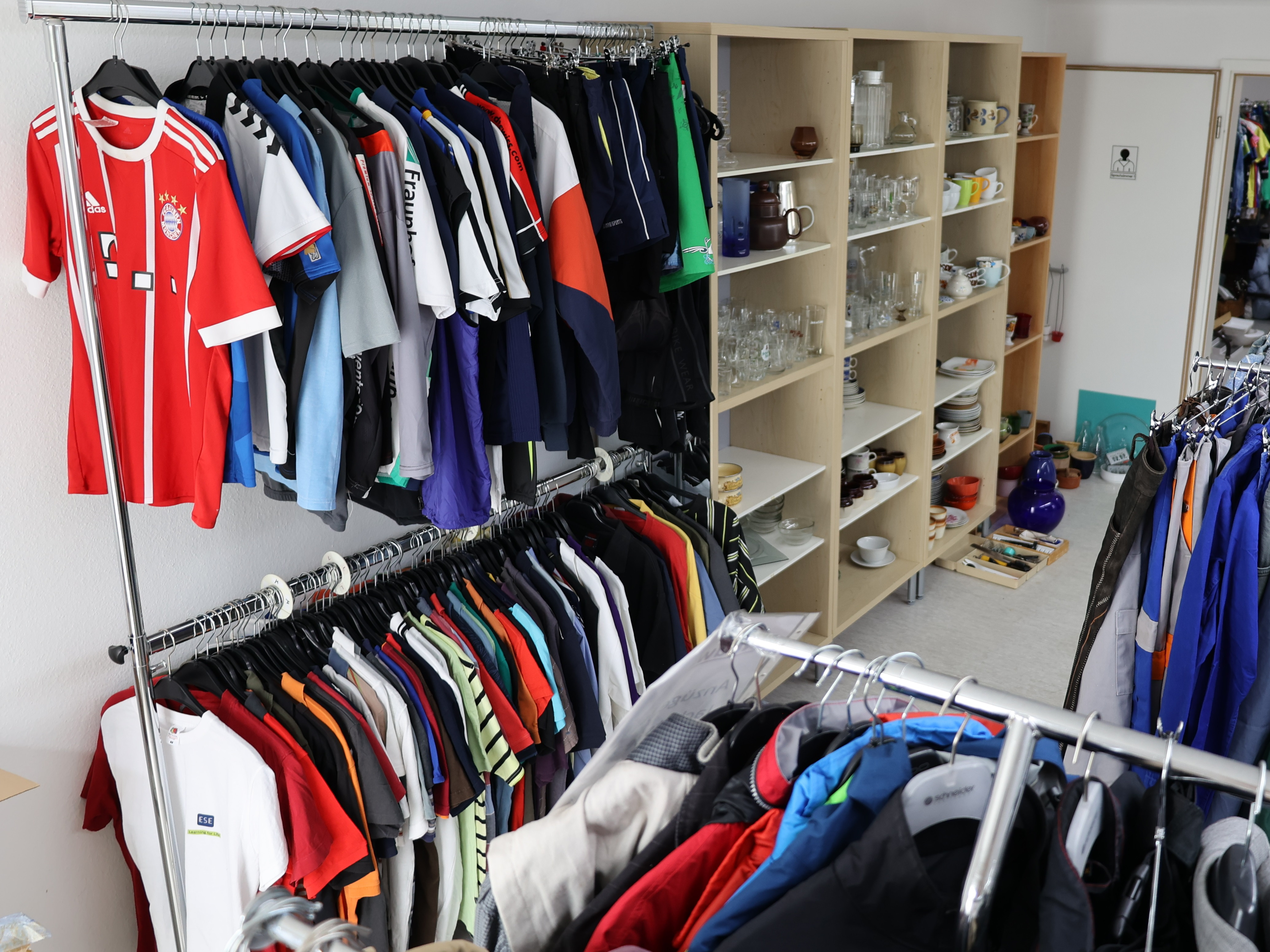  zu sehen ist ein Raum der Kleiderkammer mit gefüllten Kleiderständern und Regalen 